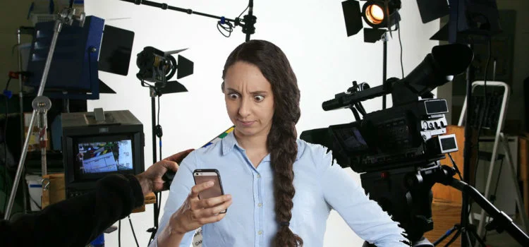 woman holding phone with camera equipment behind
